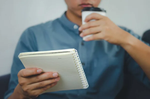 Person holding a note book and a paper coffee cup.
