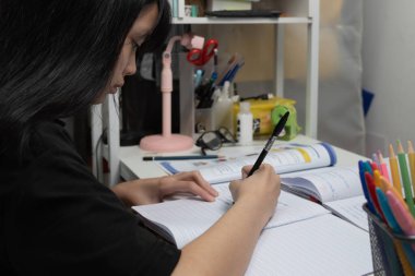 Asian student girl is writing homework and reading book at desk