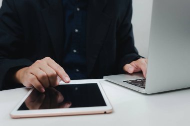 Businessman with a touch tablet and a laptop computer searches for information with Internet technology working at desk.