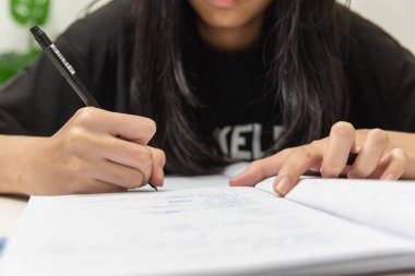 Asian student girl is writing homework and reading book at desk