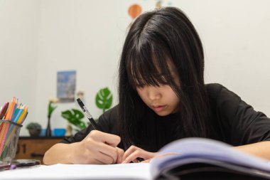 Asian student girl is writing homework and reading book at desk