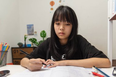 Asian student girl is writing homework and reading book at desk
