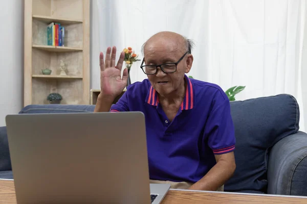 Asian elderly man sitting on the internet communication video call computer laptop at home.