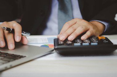 Elinde hesap makineleri ve iş belgeleri bulunan işadamı istatistiksel veri yatırım analizi ve vergi muhasebesi grafikleri tutuyor.