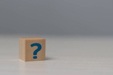 Wooden cube block shape with sign question mark symbol on table.