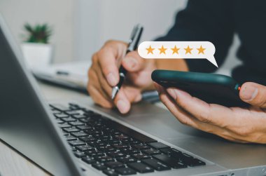 hand businessman holding smartphone and use computer laptop. Customer service feedback 5 star review satisfaction positive business concept.