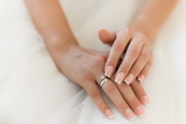 Gelinin elleri beyaz elbisedeki yüzüğü ayarlar. Nikah yüzüğü, yakın plan gelinlerin eli beyaz elbisede..
