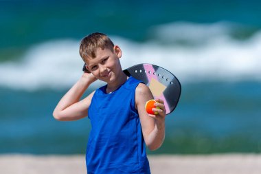 Genç çocuk sahilde tenis oynuyor. Çocuklar spor anlayışı. Yatay spor temalı poster, tebrik kartları, başlıklar, web sitesi ve uygulama