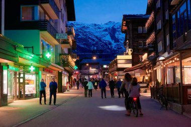 ZERMATT, SWitzERLAND - 11 Nisan 2022: Günbatımında Zermatt şehrinde gezen ve gezen turistler.