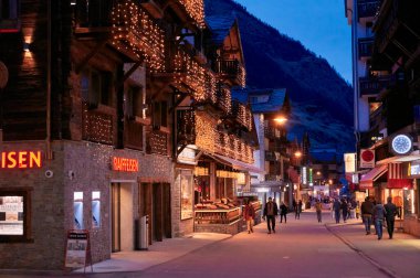 ZERMATT, SWITZERLAND - APR 11, 2022: Tourists walking and sightseeing on a street in the city of Zermatt at sunset.