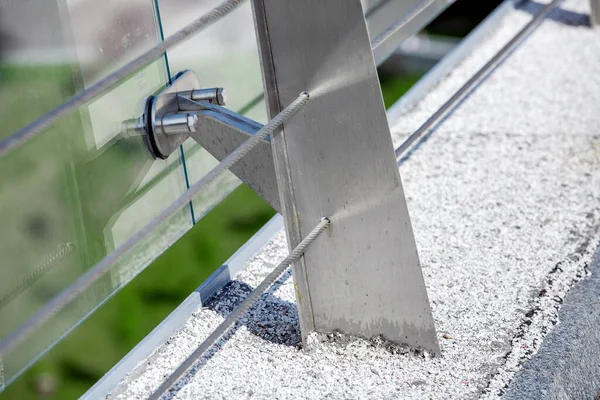 metal turnbuckles fastening of cables with steel rod on pedestrian bridge with stone pebble path and glass barrier for safety close-up details of construction on sunny day, nobody.