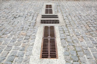 Granit taştan çakıl taşı yolda fırtına sularının drenaj ızgaraları eski şehrin paslı kanalizasyon sisteminde gelişim gösteriyor..