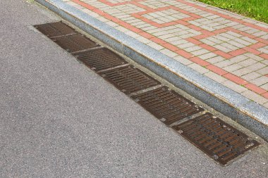 Kanalizasyon sisteminin kanalizasyon sisteminin dikdörtgen rögar delikleri yol yüzeyindeki yağmur suyunu boşaltmak için granit kaldırımda taş kiremit kaldırımlı asfalt bir yol ile.