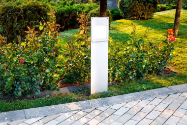 Arka bahçesinde gül çiçekleri olan düz önlü fener ve çimenlik çimenlik arazi günbatımı aydınlığıyla aydınlatılmış taş kiremit kaldırım kenarında granit kaldırımlı hiç kimse.