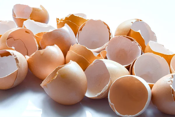 a pile of broken brown egg shells close-up, empty eggs without protein content garbage after cooking on white background.