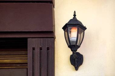Demir duvar feneri siyah renkte, cam gölgesi ve elektrik ampulü ile parıldıyor, binanın ön cephesinde kentsel duvar ışığı, lambayı yakın plan dekore edin, kimse yok..