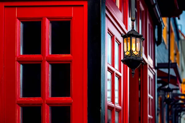 hanging iron retro lantern with a warm glow on the facade of an Asian-style wooden building with a red window frame. Architecture of the evening street lighting of city streets decorative light.