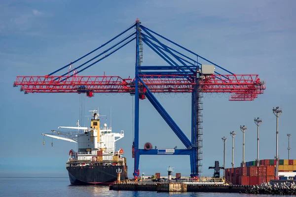 Cargo ship moored at the berth of the container ship yard for loading cargo by large cranes for unloading goods, cargo transportation by sea, shipping industry background.