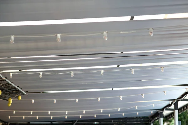 white textile ceiling of the sun shade canopy on the backyard terrace with string garlands with led bulbs suspended from the ceiling, decorative sun shade gazebo close up detail, nobody.