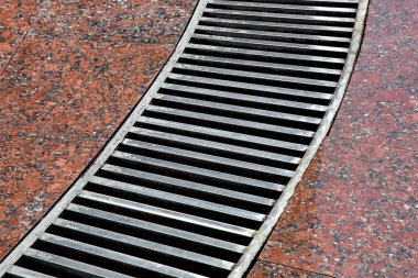 Granit zeminde ızgara çizgili kavisli drenaj sistemi, ıslak kırmızı taş granit yüzeyi, yağmurdan sonra ıslanan fırtına sisteminin yakın çekimi, hiç kimse.