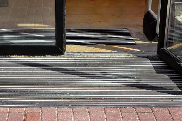 entrance to the hotel from a plink on a foot mat through a glass door, outdoor view a building close-up in sunny dry weather nobody.