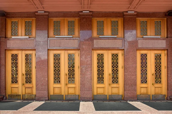 facade of old building is lined with marble entrance wooden doors and patterned glass windows rubber foot mat on threshold and decorative windows and lanterns above main entrance to business center.