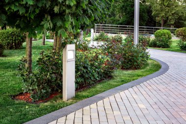 Arka bahçesinde gül çiçekleri olan düz önlü fener ve çimenlik çimenlik arazi günbatımı aydınlığıyla aydınlatılmış taş kiremit kaldırım kenarında granit kaldırımlı hiç kimse.