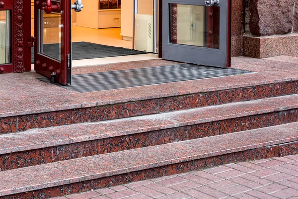 red marble staircase with granite steps to entrance door on store with glass, threshold with doormat at facade of building on retro style side view closeup, nobody.
