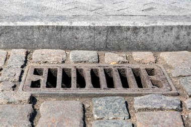 Granit kaldırım kenarındaki eski kaldırım taşlı yolda demir dikdörtgen rögar drenaj sistemi kullanılmış. Güneşli kuru havada kaldırıma yakın taş döşeme, kimse yok..