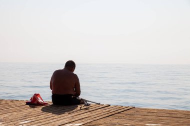 Yazın balıkçı teknesinde oltayla balık tutan bir adamın arkadan görünüşü. Emekliler için spor ve tatil