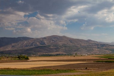 Taze hasat edilmiş saman balyaları, diğer yeşil tarlalar, dağlar ve mavi gökyüzü ile sarı kuru vadi. Koyu yeşil ağaç yaprakları. Türkiye 'de tarım ve tarım.