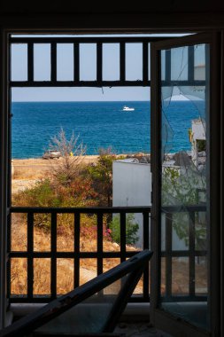 Güneşli bir yaz gününde kırık bir pencereden denize ve palmiye ağaçlarıyla sahile bakın. Zenginleri görmezden gelen fakir yaşam konsepti.