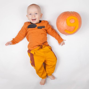 9 aylık turuncu elbiseli, gülümseyen yeni doğmuş bebek. Parlak, havadar bir çocukluk dönemi. Üzerinde 9 numara kazınmış balkabağı var..