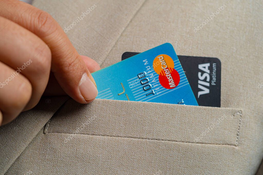 BANGKOK/THAILAND - Feb 21 : Business man pick up Visa credit cards and mastercard credit with fingers wearing in brown suit jacket and detail of the fibers of the beautiful background on 02 21 2022