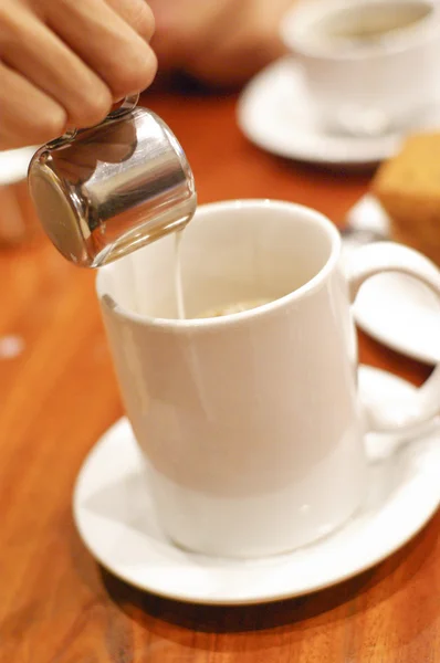 Mano dell'uomo versando latte in tazza bianca di caffè in caffè — Foto Stock