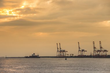Konteyner yığınları ve vinç kargo mallar için gün batımında Tersanesi