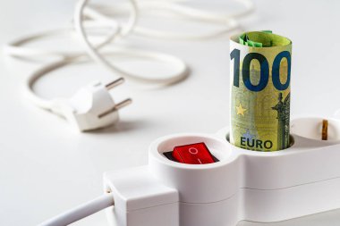 100 Euro 'luk banknotlar ve beyaz masanın üzerine elektrik prizi yerleştirilmiş uzatma soketi. Elektrik fiyatlarındaki artış, pahalı enerji, müşteriler için artan elektrik maliyeti kavramları.