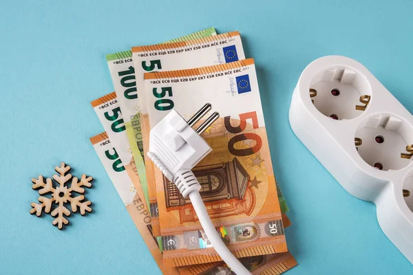 Avro banknotlarında beyaz elektrik prizi, kar tanesi ve mavi arka planda uzatma prizi. Soğuk kış mevsiminde elektrik fiyatlarında artış, elektrik maliyetlerinde artış ve pahalı enerji kavramlarında artış.