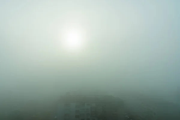 Sabah güneşi yoğun sisi zar zor aşıyor. Sokakları ve binaları kaplayan yoğun sis var. Sonbahar yoğun sisi ile kaplanmış şehir. Mevsim, sisli hava ve hava tahmini. Yüksek açı görünümü.