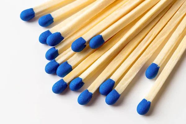 Blue wooden matches on a light gray background. Matchsticks with bright blue heads macro. Scattered wooden matches without box close-up. Design element for smoker accessory concept. Top view.