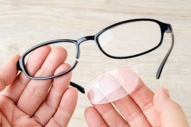 Elleri kırık jantlı ve mercekten düşmüş gözlük tutuyor. Kahverengi bir masanın üzerinde kırık mor göz telleri olan gözlük. Okuma ve bilgisayar işleri için görüş düzeltme gözlüklerinin kırılması. Üst görünüm.