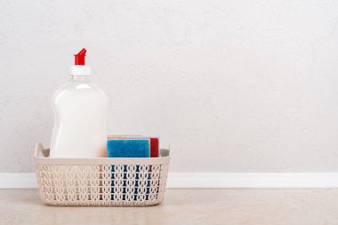 Beyaz bulaşık deterjanı ve mutfak masasındaki küçük sepetin içinde beyaz beton duvara karşı birkaç sünger. Ev yapımı mutfak deterjanı. Uzayı kopyala Ön görünüm.