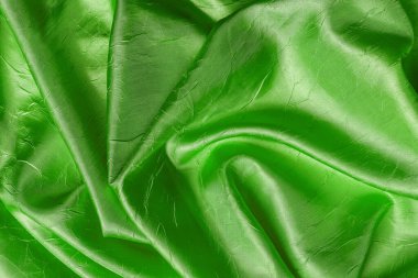 Kabarık yeşil renk dokusundan örülmüş parlak buruşuk ipek. Katlanmış zümrüt yeşili saten kumaşın arka planı. Şık lüks buruşmuş kumaş malzemesi tasarım unsuru olarak. Tam kare. Üst görünüm.