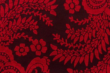 Siyah arka planda çiçek desenli kırmızı dantel kumaş. İşlemeli kırmızı ipuçlarının dokusu. Dantelli tekstil, giysi ve iç çamaşırı retro tasarımı. Soyut bağcıklı desen. Makro. Üst görünüm.