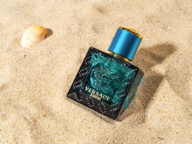 Varna, Bulgaristan, 25 Aralık 2021. Deniz kumu üzerinde dikdörtgen mavi Versace Eros parfümü şişesi. Gianni Versace lüks moda şirketi tarafından üretilen şık erkek parfümü. Üst görünüm.