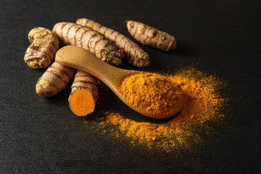 Tahta kaşıkta organik zerdeçal tozu ve siyah bir arka planda çiğ sokağa çıkma yasağı kökleri. Körcuma longa linn 'in taze ve zemin rizomları. Hint baharatı ve doğal antioksidan. Alçakgönüllülük. Ön görünüm.