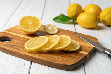 Kahverengi kesme tahtasında beyaz ahşap masanın üzerinde taze limon dilimleri. Citruces 'i bıçakla kesmek. Süper yiyecekler için çiğ limon, antioksidan ve sağlıklı beslenme konseptleri için vitamin. Ön görünüm.