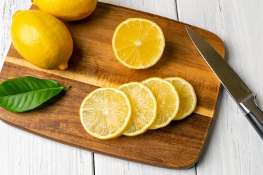 Kahverengi ahşap doğrama tahtasında tam limon ve sulu dilimler. Citruces 'i bıçakla kesmek. C vitamini için çiğ limon, antioksidan, yemek pişirme ve sağlıklı yeme kavramları. Ekşi meyve tadı. Üst görünüm.