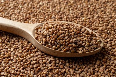 Tahta kaşık ve çiğ kepekli karabuğday yakından yetişir. Kızarmış organik karabuğday taneleri. Glütensiz beslenme, vejetaryen yiyecekler ve diyet lif kavramları için gerekli malzemeler. Ön görünüm.