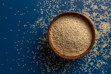 Kahverengi ahşap bir kasede kurumuş kinoa ve dağınık tanecikler. Glütensiz diyet için beyaz kinoa tohumu. Superfood chenopodium kinoası. Vejetaryen sağlıklı beslenme. Uzayı kopyala Üst görünüm.